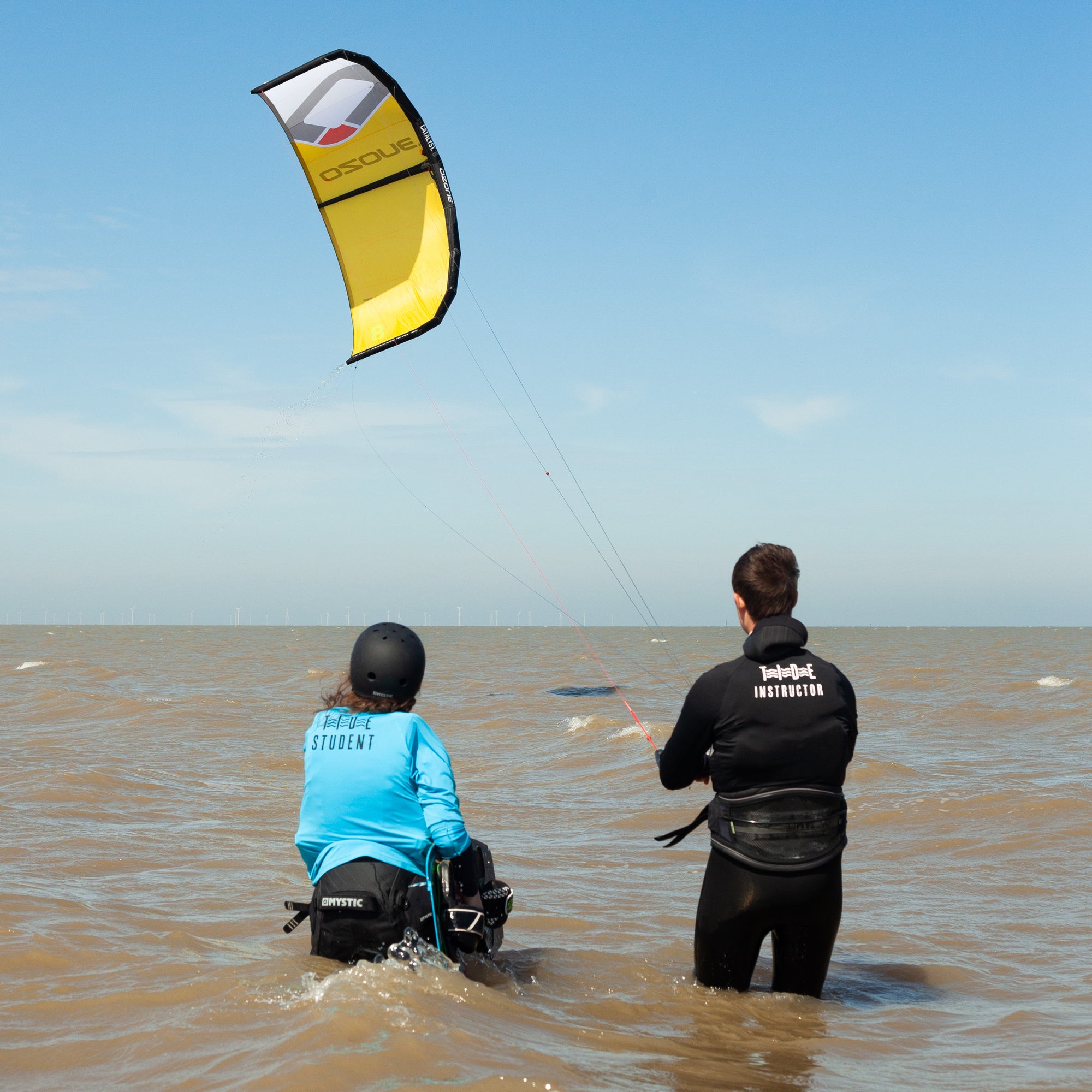 Kitesurfing instructor teaching student learning to kite  in the water whilst flying a kite.