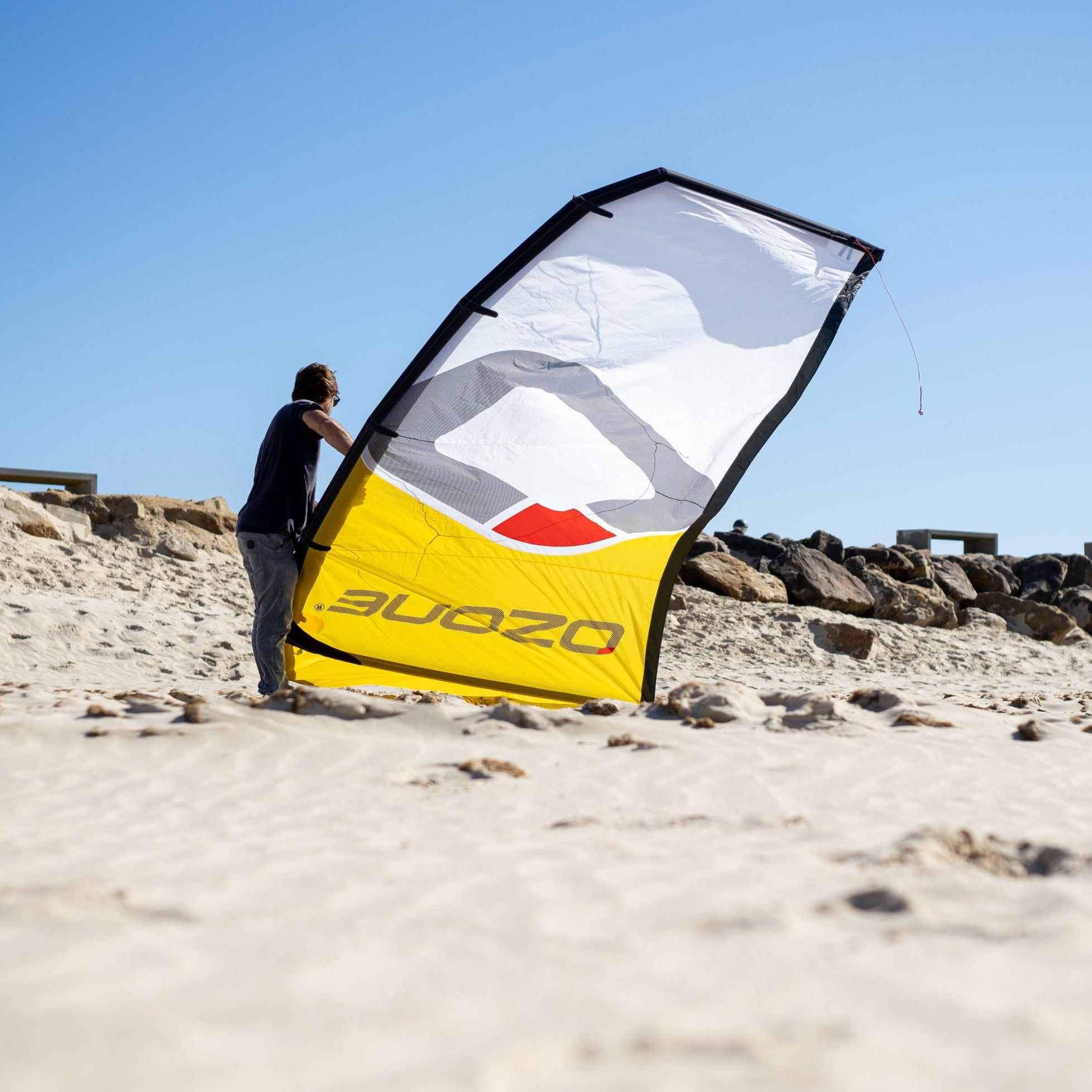 A kitesurfer pumping up the yellow Ozone Catalyst V3 on a sandy beach.
