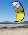The Ozone Catalyst V3 in yellow flying above a beach in clear blue sky.