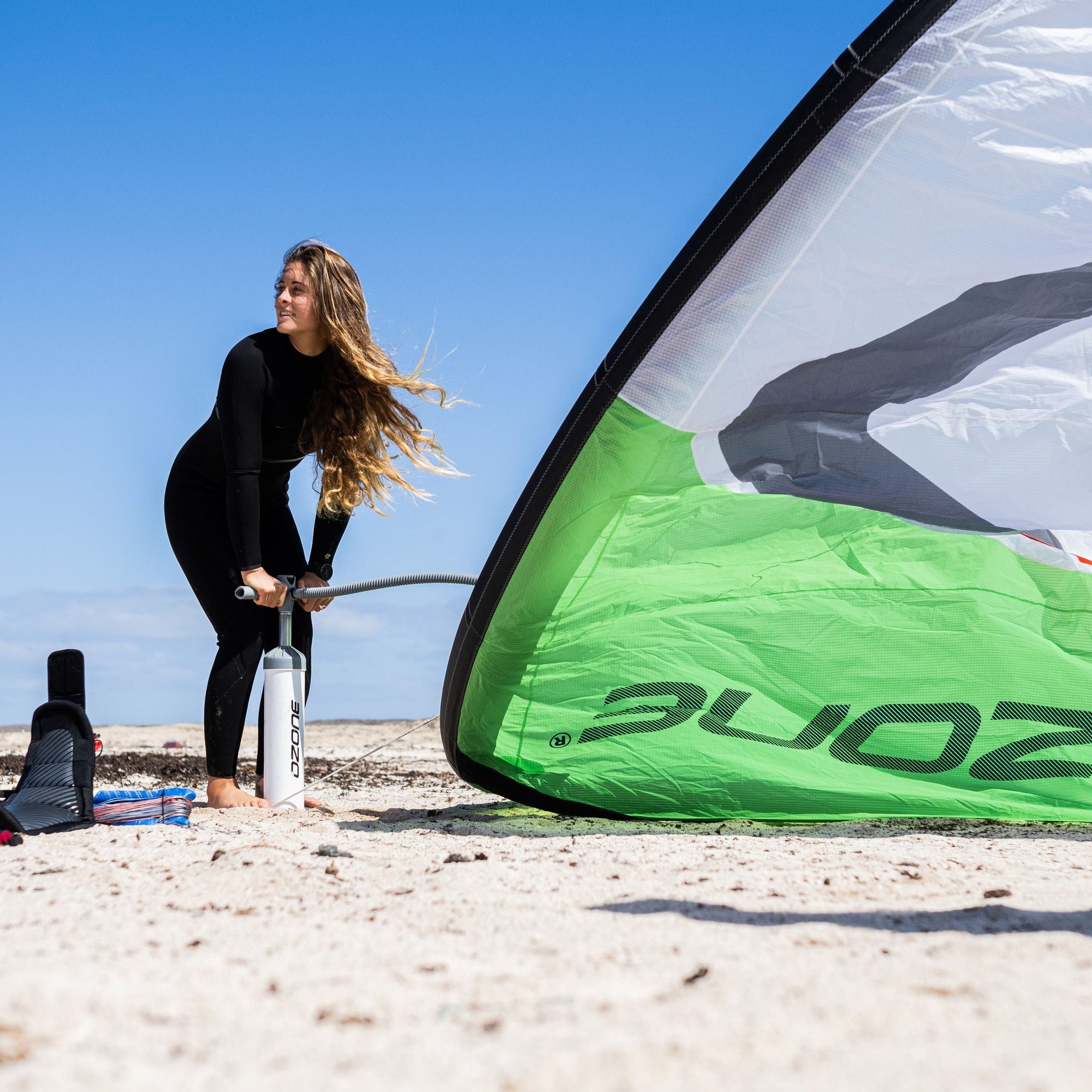 Person pumping up a green Ozone Alpha V2 on a sandy beach